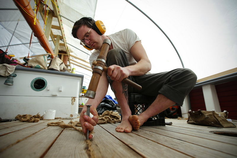 Garett Eisele, of Clark & Eisele Traditional Boatbuilding, uses a mallet and a calking iron, to install new tarred hemp fiber into the gaps between the planks on the foredeck of the Ernestina-Morrissey schooner docked at State Pier in New Bedford, MA. PHOTO PETER PEREIRA