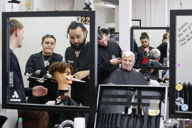 Rob Roy Academy instructor Lucas Hernandez is reflected in the mirror on the left as he inspects a preparation test being performed by a student, in the background Nathan Dorego gives Joe Correia a haircut at the Rob Roy Academy barber school in Fall River, MA.  PHOTO PETER PEREIRA