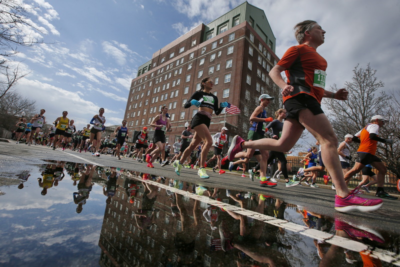 Runners are reflected in a puddle, as them make their way up Pleasant Street past the old New Bedford Hotel during the 2024 New Bedford Half Marathon.  PHOTO PETER PEREIRA