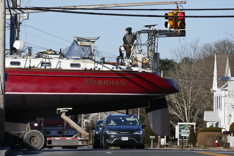 Traffic looks on as Jason Costa of Triad Boatworks rides the sailboat Meridian while crossing Route 6 in Mattapoisett, MA to put it in the water. 