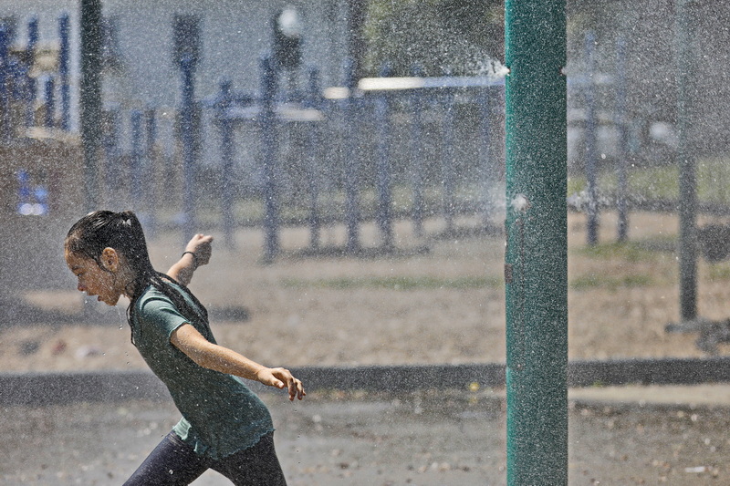 A girl runs through the fine water mist thrown up by the sprinklers at Clasky Common Park in New Bedford, MA on a sweltering day. PHOTO PETER PEREIRA