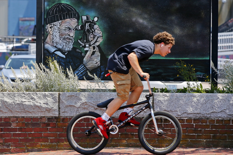 A young man rides his bicycle up MacArthur Drive in New Bedford, MA past a painting of a sailor using a sextant.  PHOTO PETER PEREIRA