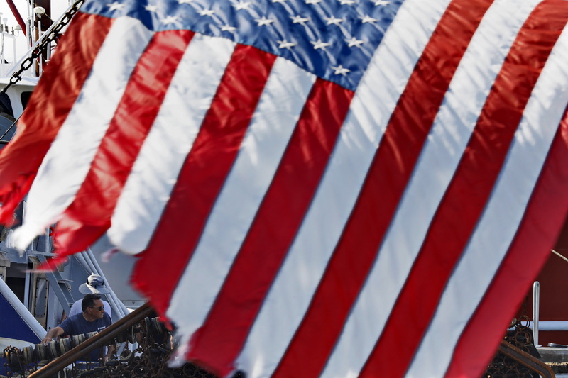 A fisherman on a scalloper tied in New Bedord harbor is seen behind the American flag hanging from the stern of the schooner Ernestina-Morrissey at State Pier.  PHOTO PETER PEREIRA