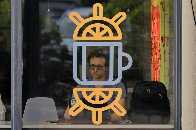 A patron of Ground Floor Coffee in New Bedford, MA is framed by a coffee cup on the window as he enjoys a beverage while operating his laptop.  PHOTO PETER PEREIRA