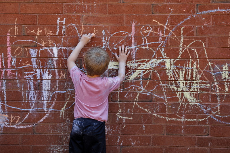 A young boy in the YMCA Child Care program in downtown New Bedford, MA lets his creativity flow with caulk on the building's red brick wall. PHOTO PETER PEREIRA