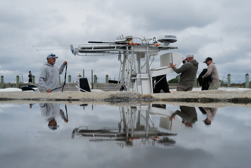 Three men are reflected on a puddle on the wharf as they cast off from Mattapoisett, MA for a day of boating. PHOTO PETER PEREIRA