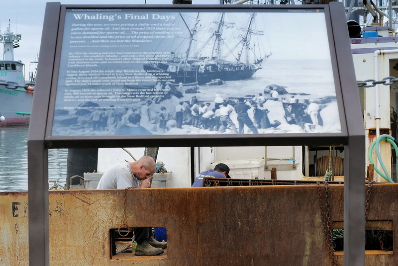 A fisherman takes a break after repairing the dredges on a fishing boat docked in New Bedford.  The placard outlines the Wanderer, the last whaling ship which left from this spont in New Bedford, MA and sank exactly 100 years ago in Cuttyhunk during a storm. PHOTO PETER PEREIRA