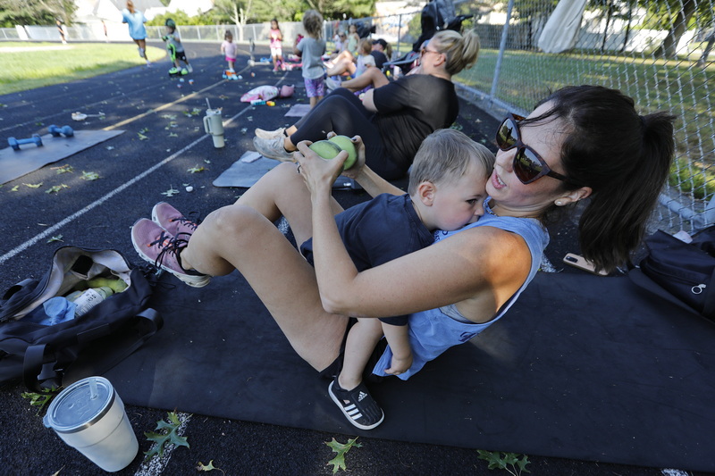 Sarah Freshman tries to work with weights as her son Wesley Freshman, 1, rests on her chest during the I Stroll Southcoast weekly workout session at Cushman Park in Fairhaven, MA for mom with young children who want to work out.  PHOTO PETER PEREIRA