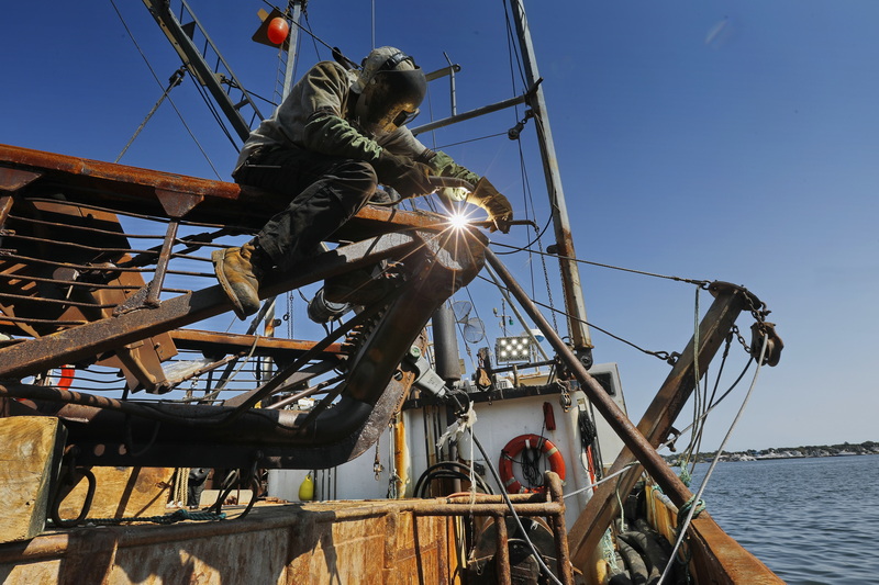 Chris Macedo of Macedo Welding finds himself perched atop a dredge as he makes repairs to the skid plats of the sea clam fishing boat docked in New Bedford, MA.  PHOTO PETER PEREIRA