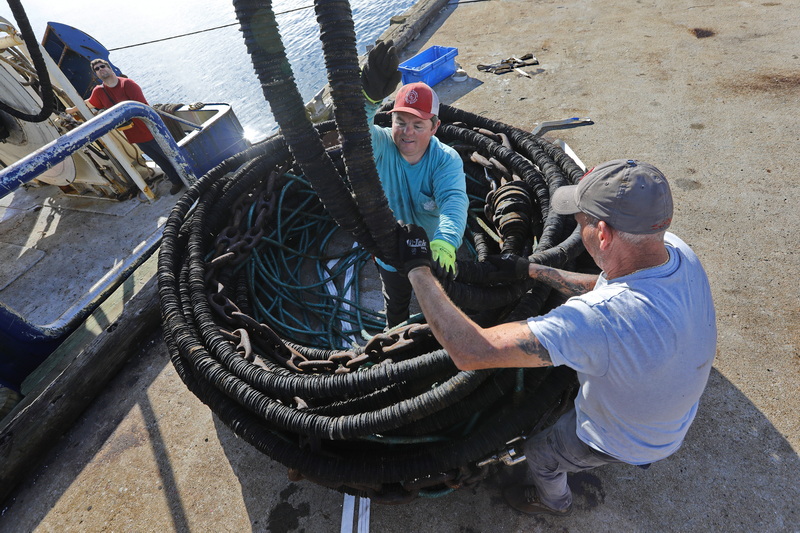 Captain Rory Mullen, left, operates the winch as Gabe Folan finds himself surrounded by the squid gear he and Mike Lawless are winding into a coil on State Pier in New Bedford, MA in preparation for replacing it with herring catching nets aboard the fishing boat Enterprise. PHOTO PETER PEREIRA