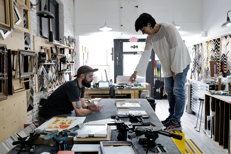 Irene Rodriguez stands on a step ladder to get a better look at the custom framing that she and Nick Martin, owner, are preparing for the photographs she is having framed at Art Box Custom Framing on Union Street in New Bedford, MA. PHOTO PETER PEREIRA