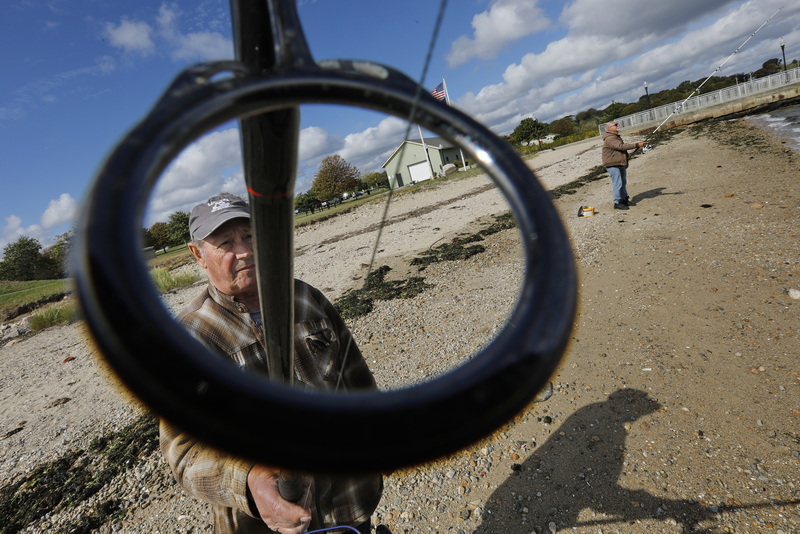 With finger on the line, Arlindo Vitorino is seen through one of the guides on his fishing rod as he and Herve Fernandes are seen fishing at Fort Taber Park in New Bedford, MA. PHOTO PETER PEREIRA