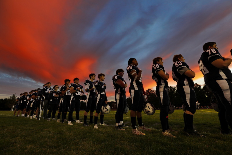 The sun sets in the distance as Apponequet Regional High School players listen to the National Anthem before playing Dartmouth High School on Friday night football in Lakeville, MA.  PHOTO PETER PEREIRA