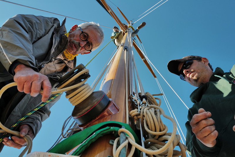 Joe Mello, left, and Jason Costa, right, of Triad Boatworks remove the rigging from the mast of a sailboat docked in Mattapoisett, MA as Silas Costa looks down from above as he sets up a strap to remove the mast. PHOTO PETER PEREIRA