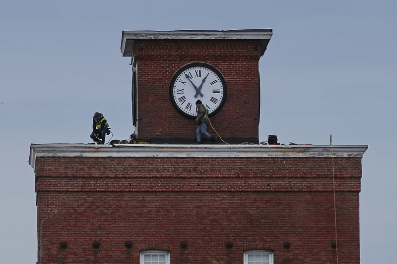 Roofers walk past the iconic clock atop the Wamsutta Place as they install a new roof on the old mill which has been converted into apartments in New Bedford, MA. PHOTO PETER PEREIRA