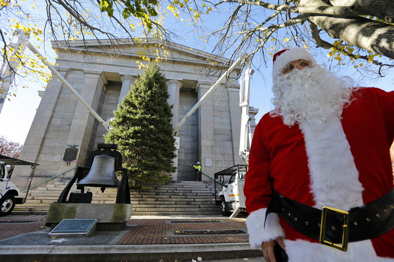 Santa (Nicholas Riquinha, New Bedford Highway Department driver of the truck which carried the tree) looks on as New Bedford Highway Department and Greenspace crews place the 2024 Christmas tree into position in front of the New Bedford Public Library. PHOTO PETER PEREIRA