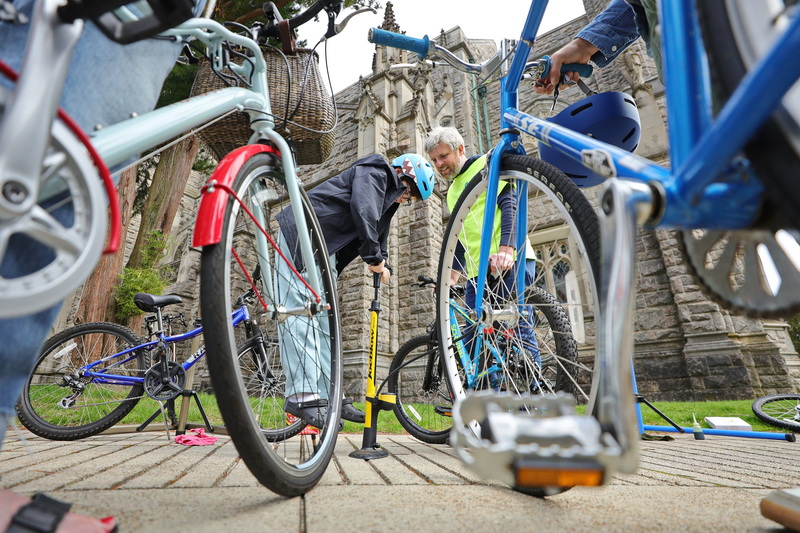 Adam Wells looks on as Teddy Arruda, 10, is lifted into the air as he attempts to fill the tire on his bicycle during the Blessing of the Bikes event hosted by the Unitarian Universalist Society Fairhaven, SouthCoast Places for People and Youth Opportunities Unlimited.  Volunteer bicycle mechanics offered to make repairs to any community members who brought their bicycle to the event at the Unitarian Memorial Church in Fairhaven, MA. PHOTO PETER PEREIRA