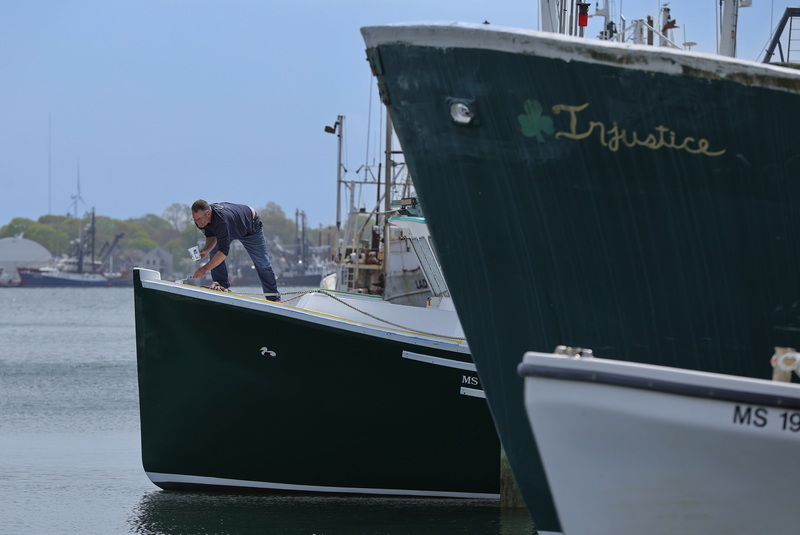 A man paints the bow of a lobster boat docked in New Bedford, MA. PHOTO PETER PEREIRA