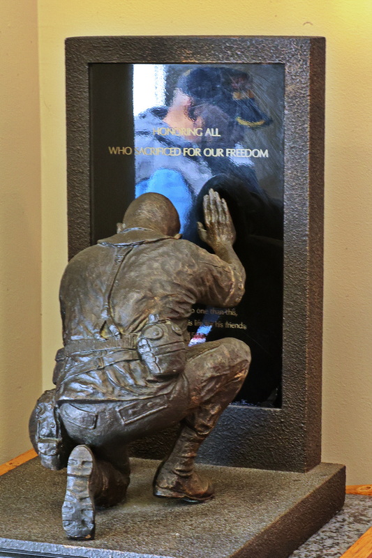 In the waiting area of the Veterans Transition House in New Bedford, MA a statue appears to extend its hand toward a veteran whose reflection is visible in the panel. PHOTO PETER PEREIRA