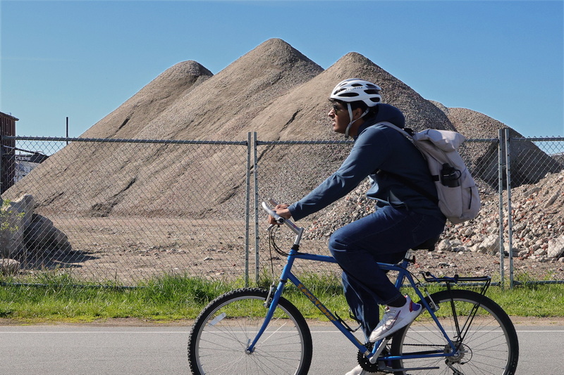 A man riding his bicycle on Gifford Street in New Bedford, MA appears to be riding past the great pyramids of Egypt, which are actually piles of dirt from a mill demolition happening in the background. PHOTO PETER PEREIRA
