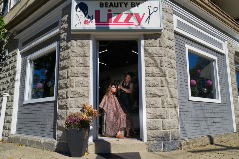Liz Sousa performs a keratin hair treatment on Gloria Paiva at the entrance of her hair salon Beauty by Lizzy at the corner of Highland Street and Durfee Street in New Bedford, MA on October 15, 2026, to prevent her smoke detector from being triggered by the steam dryer required for the treatment. PHOTO PETER PEREIRA