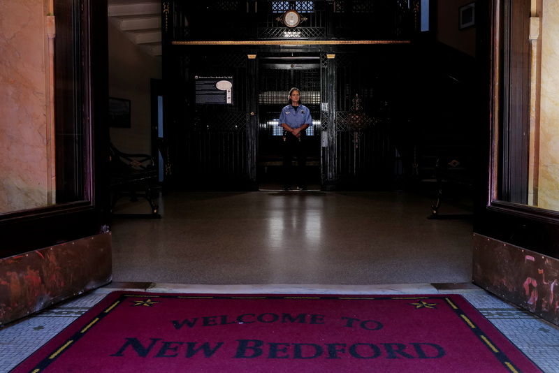 At New Bedford City Hall on October 16, 2026, elevator operator JoAnn Perry waits beneath the light by the entrance to the oldest operating elevator in the United States, ready to take visitors to the historic building�s upper floors. PHOTO PETER PEREIRA