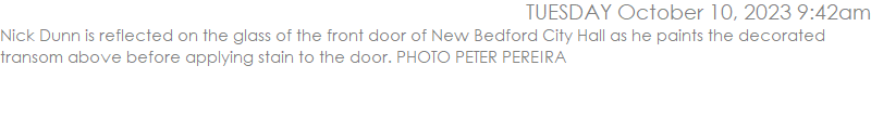 Nick Dunn is reflected on the glass of the front door of New Bedford City Hall as he paints the decorated transom above before applying stain to the door. PHOTO PETER PEREIRA
