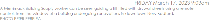 A Merrimack Building Supply worker can be seen guiding a lift filled with drywall sheets using a remote control, from the window of a building undergoing renovations in downtown New Bedford. 